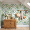 Sigrid Sage Nordic Botanical Wallpaper in 52 inch repeat styled in an attic mudroom with wood cabinet, coat hooks, woven basket, and larger sage botanical pattern