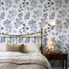 Angelique Blue Floral Wallpaper in 26 inch repeat styled in a Victorian bedroom with brass bed, wood nightstand, wall sconce, and large blue floral wall decor