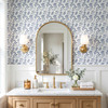 Angelique Blue Floral Wallpaper in 6.5 inch repeat styled in a bathroom vanity with gold mirror, brass sconces, wood cabinet, and medium blue floral pattern