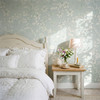 Celia Mint Botanical Wallpaper styled in a cottage bedroom with white bedding, wood nightstand, flowers, soft sunlight, and mint green botanical wallpaper