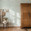 Celia Mint Botanical Wallpaper styled in a farmhouse bedroom with vintage wood armoire, chair, wall hooks, flowers, and soft mint floral wall decor