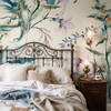 Eden Watercolor Floral Wallpaper styled in a Victorian bedroom with brass bed, wood nightstand, layered bedding, wall sconce, and oversized botanical floral wallpaper
