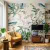Eden Watercolor Floral Wallpaper styled in a bohemian living room with yellow chair, plants, media cabinet, colorful rug, and oversized botanical floral wall decor