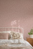 Soft blush pink leaf botanical wallpaper in a cozy girls bedroom with neutral bedding and floral pillow