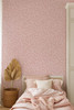 Blush pink botanical wallpaper in a feminine bedroom with layered pink bedding, woven basket and natural decor
