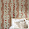 Close-up of Elsie Sunbaked Clay floral stripe wallpaper above a woven bedroom headboard, 52 inch repeat