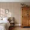 Elsie Sunbaked Clay floral stripe wallpaper behind a bed and wood armoire, 13 inch repeat