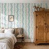 Elsie Aquamarine light teal floral stripe wallpaper behind a bed and warm wood armoire, 52 inch repeat