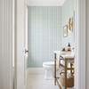 Delicate light teal stripes of Elsie Aquamarine wallpaper in a bathroom with a wood vanity, 13 inch repeat