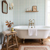 Small-scale Elsie Aquamarine light teal wallpaper behind a white bathtub and wooden stool, 13 inch repeat