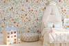 Madison floral wallpaper wraps a child’s bedroom with a cream canopy bed, pastel dollhouse and round floor cushion.