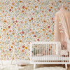 Madison floral nursery wallpaper in pink, golden yellow and sage green behind a white crib, with a blush canopy and a small white chair.