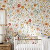 Madison floral wallpaper with pink and coral flowers, yellow blossoms and sage foliage behind a brass crib beside a wooden chest and white lamp.