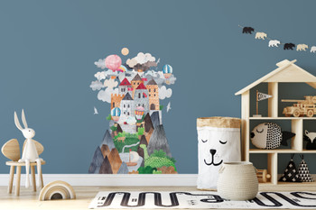 Watercolor castle mountain wall decal displayed on a blue playroom wall above toys and a wooden dollhouse