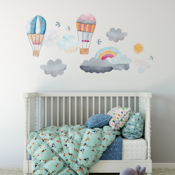 Watercolor hot air balloon, clouds and rainbow wall decal set displayed above a white nursery crib with teal bedding