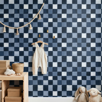 Blue checkered wallpaper in a nursery or kids room with white beadboard, brass hooks, and baby clothes