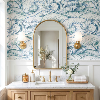Marina blue Atlantic wave wallpaper in 52 inch repeat styled in a bathroom with gold arch mirror, brass sconces, white wainscoting, and wood vanity