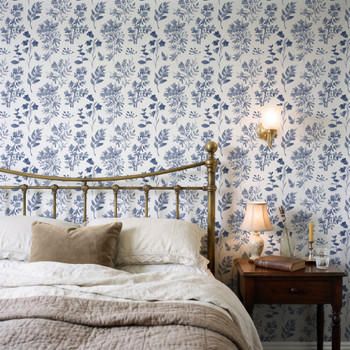 Angelique Blue Floral Wallpaper in 13 inch repeat styled in a Victorian bedroom with brass bed, wood nightstand, wall sconce, and delicate blue botanical pattern