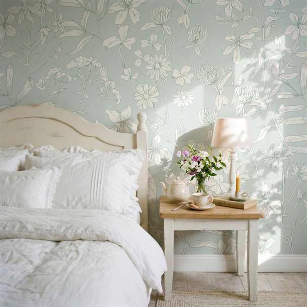 Celia Mint Botanical Wallpaper styled in a soft cottage bedroom with white bedding, wood nightstand, flowers, and large mint floral line art wall pattern