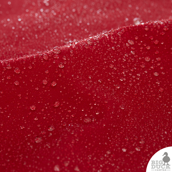 Water droplets beading on Red waxed canvas surface, demonstrating its water-repellent, non-toxic wax coating and dense cotton weave