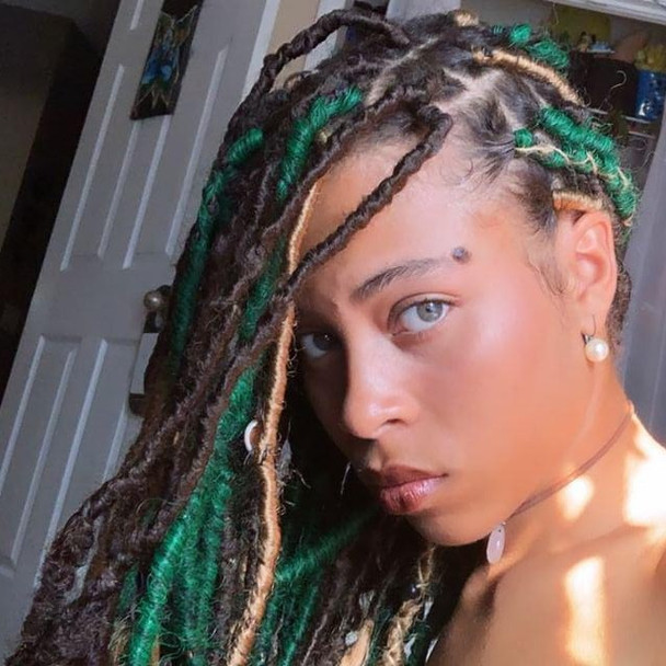 Raine wearing faux locs made from marley braid in 6 Chestnut Brown, 27 Strawberry Blond, and 1B Off Black/Emerald Green Mix