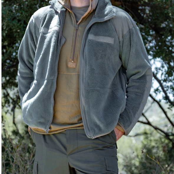 Man in the woods standing with his hands in his pocket wearing the Foliage PolarTec Fleece Jacket Man in the woods standing with his hands in his pocket wearing the Foliage PolarTec Fleece Jacket