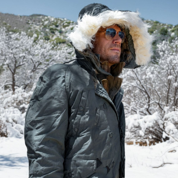 Man wearing a military N3B parka with the hood in use and a background of snow and a mountain Man wearing a military N3B parka with the hood in use and a background of snow and a mountain