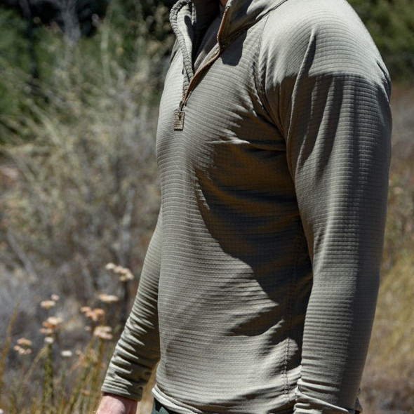 Man in the grass with his left side showing wearing the Grid Fleece Top ECWCS Gen III Man in the grass with his left side showing wearing the Grid Fleece Top ECWCS Gen III