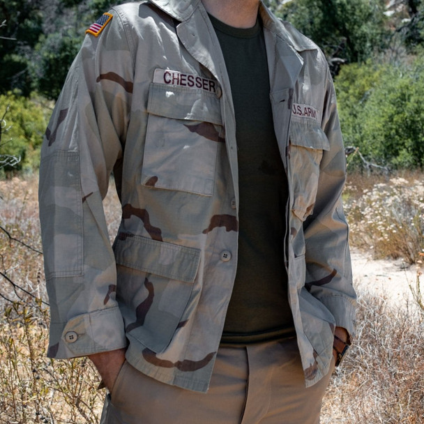 Man standing in gross with left hand in pocket wearing the U.S. Issue 3 Color Desert BDU Shirt, Used