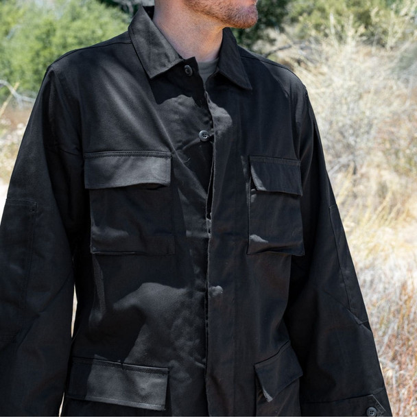 Man standing in the woods looking to the left wearing the Black BDU jacket shirt