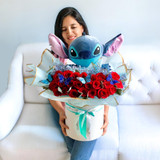 A floral arrangement with red roses and a Stitch plush bear in a white box hold by a lady seated on a white sofa.