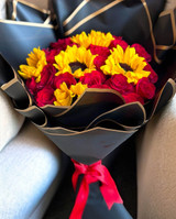 A bouquet of red roses and sunflowers wrapped in a black paper.