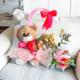 A set of a teddy bear, tulips bouquet and chocolates in a clear purse on a white sofa.