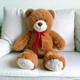 A brown jumbo teddy bear seated on a white sofa.