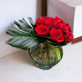 a bunch of red roses white tropical leaves in a crystal vase.