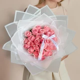 Woman holding a luxury bouquet of 24 premium pink roses wrapped in elegant white translucent paper against a soft neutral background.