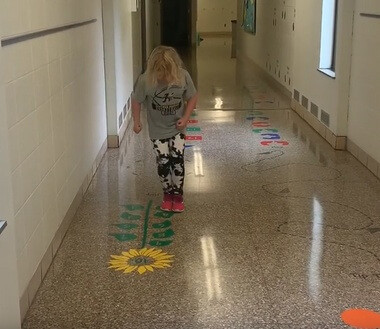 Sensory Path Floor Decal Sunflower Hopscotch School Activity Sticker — A child walking on a colorful, decorated school