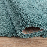 plain shaggy duck egg circle rug folded on wooden floor