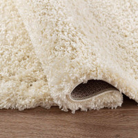 plain shaggy ivory circle rug folded on wooden floor