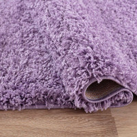 plain shaggy lilac circle rug folded on wooden floor