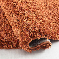 plain shaggy terracotta circle rug folded on a wooden floor