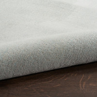 grey seafoam abstract rug partially rolled on a dark wood floor