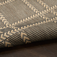 charcoal geometric indoor outdoor rug partially rolled on wood floor