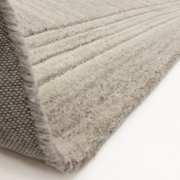 The underside and premium heavy canvas backing of a soft grey tufted wool area rug flipped at the corner.