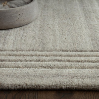 Detailed view of a light grey wool rug with a linear cream border layout, styled next to a rustic concrete decor bowl.