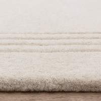 Close-up profile of a plush ivory wool rug featuring a three-line charcoal grey accent border on a light wood floor.