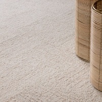 Corner detail of a geometric white and sand wool rug, styled next to modern neutral decor containers on hardwood flooring.