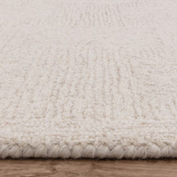 Close-up profile of the white and sand wool rug edge, highlighting the thick, woven pile texture and neat monochrome border.