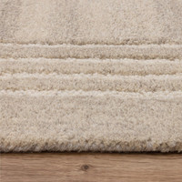Close-up profile of the Orlo sand beige wool rug showing its thick plush texture and dark grey triple pinstripe border on a light wood floor.