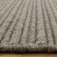 Side view detail of a textured neutral wool rug highlighting its thick, durable linear construction.